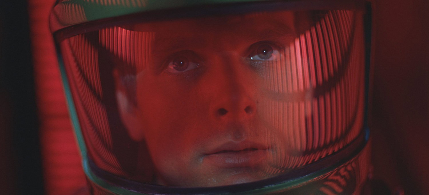 Primo piano di David Bowman nel casco spaziale, con riflessi luminosi sul viso