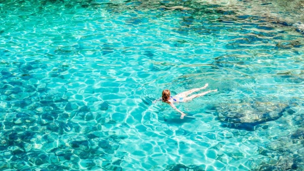 Persona immersa nell'acqua cristallina della piscina naturale della Grotta della poesia in Salento